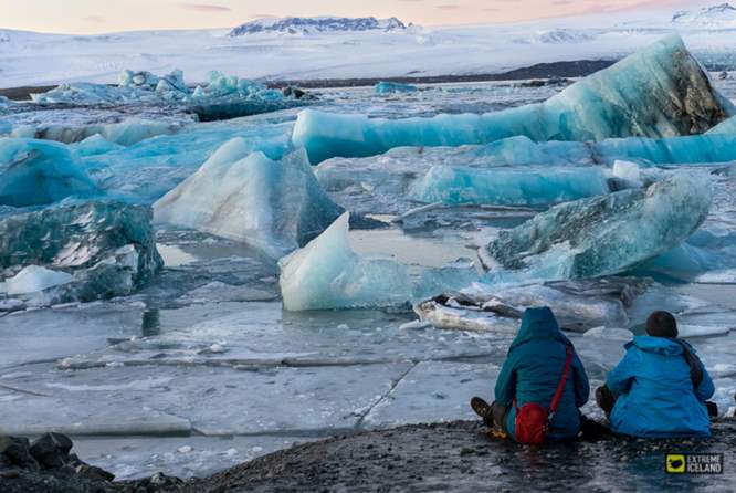 2位游客坐在冰湖岸边